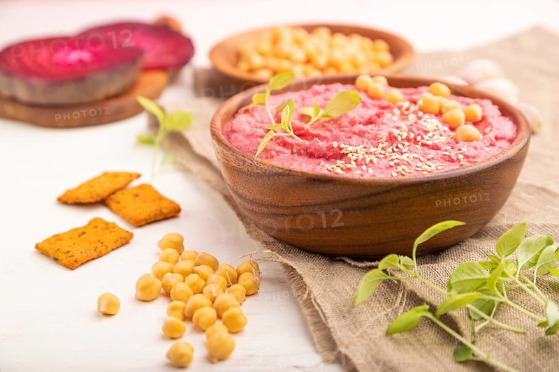 Hummus with beet and microgreen basil sprouts in wooden bowl on a white wooden background and linen textile. Side view, close up, selective focus