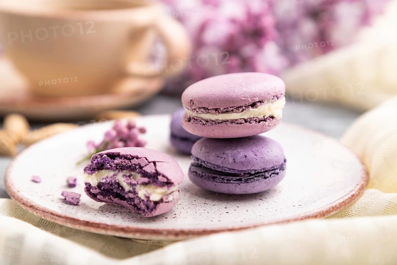 Purple macarons or macaroons cakes with cup of coffee on a gray wooden background and white linen textile. Side view, close up, selective focus