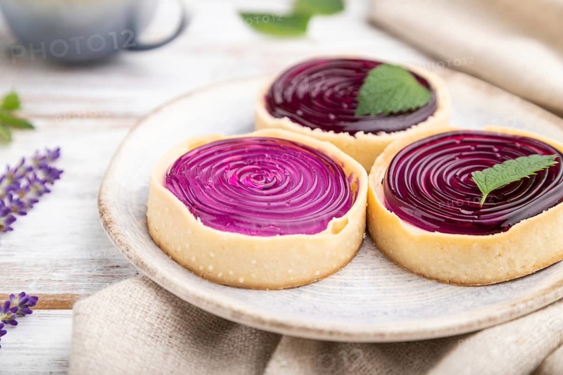 Sweet tartlets with jelly and milk cream with cup of coffee on a white wooden background and linen textile. Side view, close up, selective focus