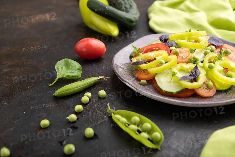 Vegetarian salad from green pea, tomatoes, pepper and basil on a black concrete background and green textile. Side view, close up, selective focus