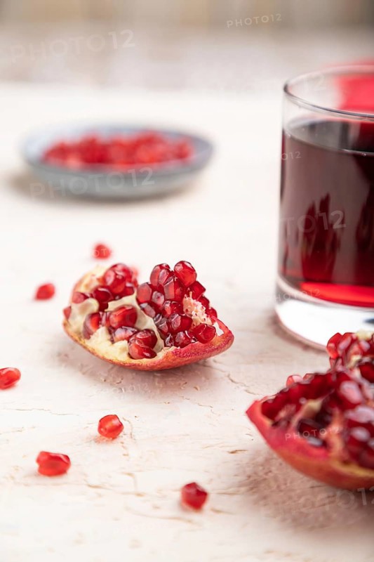 Glass of pomegranate juice on a white concrete background with red textile. Side view, close up, selective focus