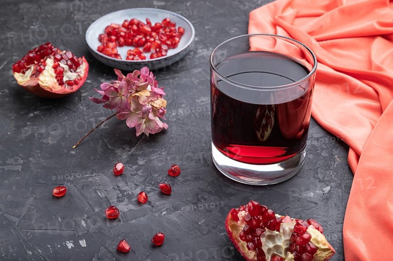 Glass of pomegranate juice on a black concrete background with red textile. Side view, close up