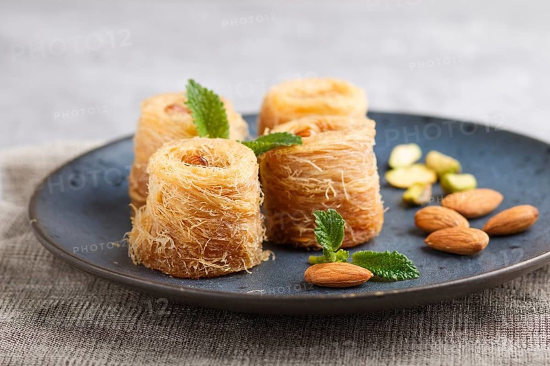 Kunafa, traditional arabic sweets in blue ceramic plate on a gray concrete background. side view, close up, selective focus
