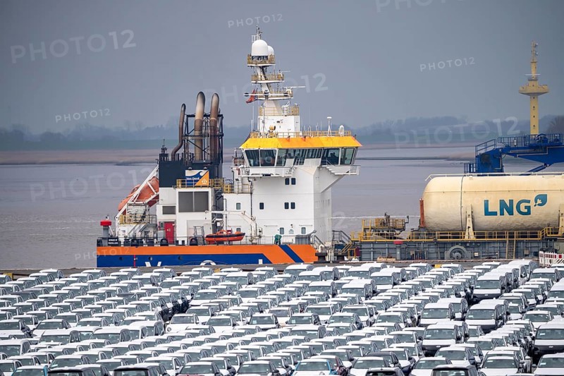 Parking space for import vehicles, hundreds of Hyundai Ioniq, electric cars, waiting for onward transport, behind them, on the Weser, the dredger, the hopper dredger, suction dredger, Vox Ariane, which holds the tug to a certain depth, at the EUROGATE container terminal in the overseas port of Bremerhaven, Lower Saxony, Germany, Europe