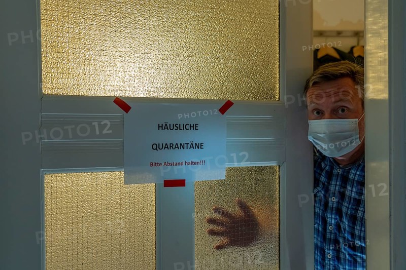 Symbolic image Domestic quarantine, man is in isolation at home due to a suspected corona infection, warning sign for visitors on the front door, communicating with a visitor through the door