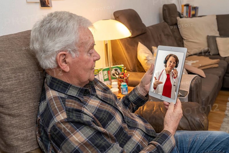 Symbolic image of telemedicine, elderly patient speaking to a doctor in a video conference from home