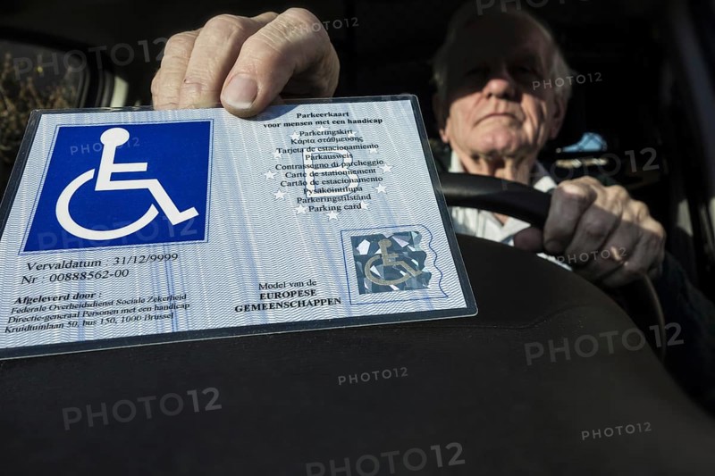 Handicapped elderly man placing EU parking card for people with disabilities ? Blue Badge, standardized across the EU and EEA, behind windscreen of car