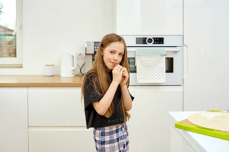 Young funny girl bites a piece of fresh flatbread in the kitchen
