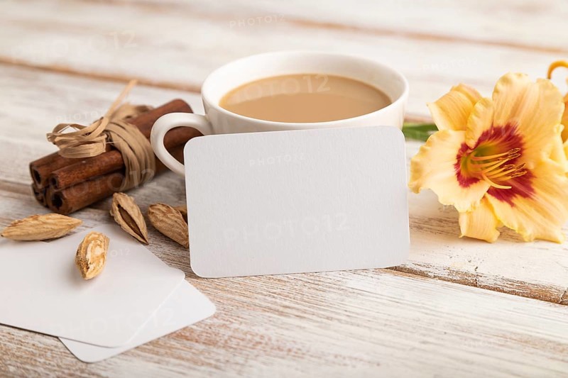White paper business card mockup with orange day-lily flower and cup of coffee on white wooden background. Blank, side view, copy space, still life. spring concept