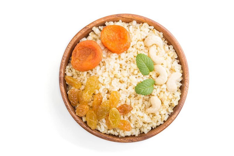 Bulgur porridge with dried apricots, raisins and cashew in wooden bowl isolated on white background. Top view, flat lay, close up. Turkish traditional cuisine