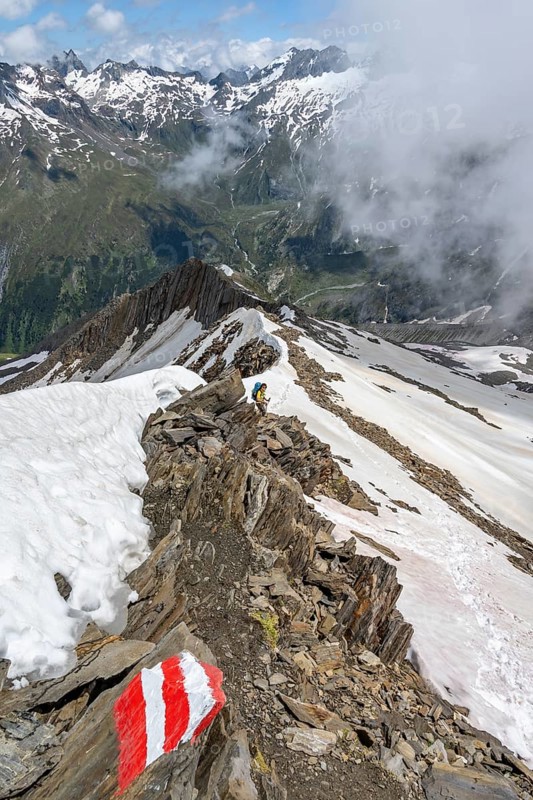 Mountaineer on a rocky ridge with snow, descent from the summit of Schönbichler Horn, view of snow-covered mountain peaks and valley Zemmgrund, Berliner Höhenweg, Zillertal Alps, Tyrol, Austria, Europe