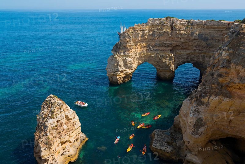 Stone arches and rocks jut out of the clear blue sea, kayaks and a small boat glide across the water, Praia da Marinha, double rock arch, Lagoa, Rocky Algarve, Algarve, Portugal, Europe