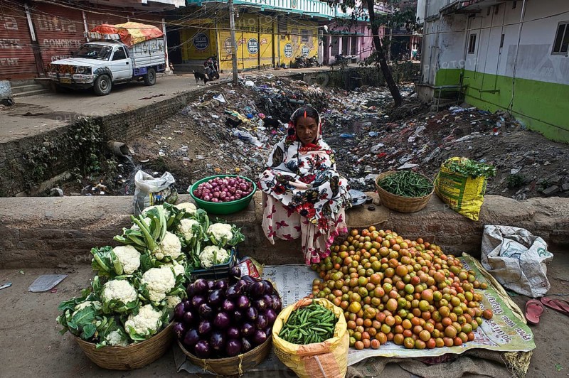 Vegetable seller in a street at Bodhgaya, India. Sewer is visible behind the woman