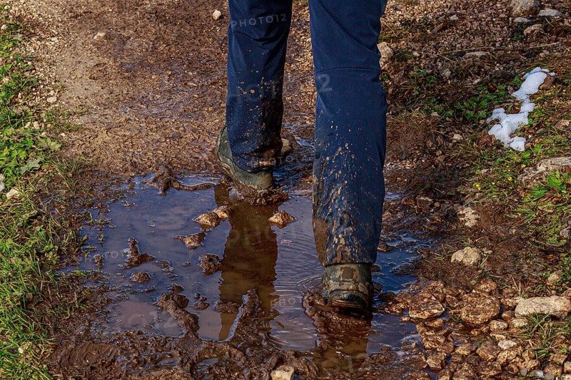 A person walks on a muddy path with puddles of water and wet sections