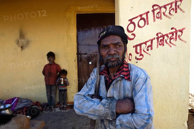 Portrait of a man and children belonging to the Birhor tribe, Jharkhand, India. They are standing in front of the one room house that the Indian government has built for them. The name of the owner is written in red on the wall. Formerly, Birhor were nomads, they were living on hunting and gathering. After the Indian independence in 1947, the government has tried to settle them by giving them lands and bullocks. But for many of them, this integration attempt has failed. They are now living in dire poverty