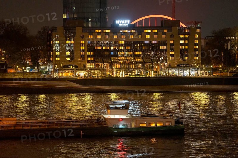 The Hyatt Regency Hotel on the Rhine, in Cologne Deutz, behind it the illuminated arch of the Lanxess Arena, cargo ship on the Rhine, North Rhine-Westphalia, Germany, Europe