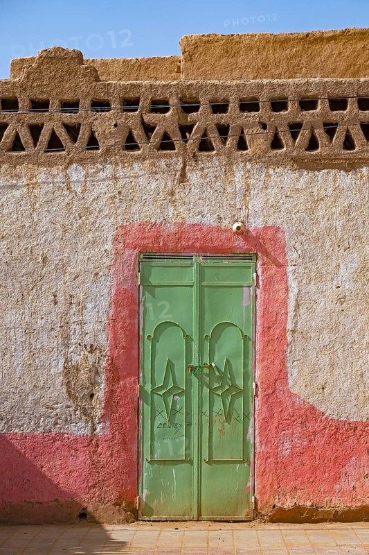 Green iron door in wall of traditional house made of mud and straw in the village Merzouga in the Sahara Desert, Drâa-Tafilalet, Errachidia, Morocco, Africa