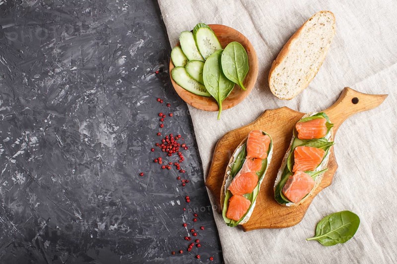 Smoked salmon sandwiches with cucumber and spinach on wooden board on a black concrete background. top view, copy space