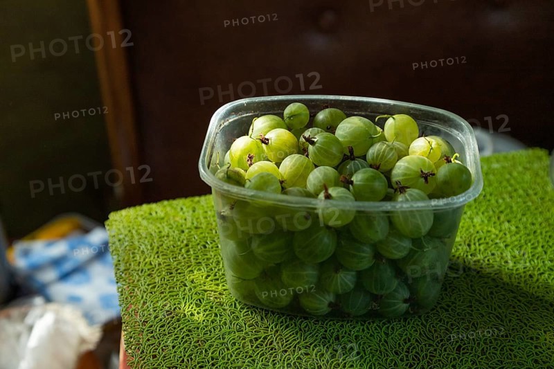 Plastic container with green gooseberries on the kitchen table. side view, close up, natural light, shadows