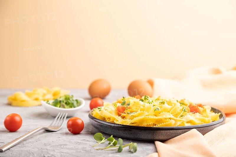 Reginelle semolina pasta with tomato, eggs and microgreen sprouts on a gray and orange background and orange textile. Side view, selective focus
