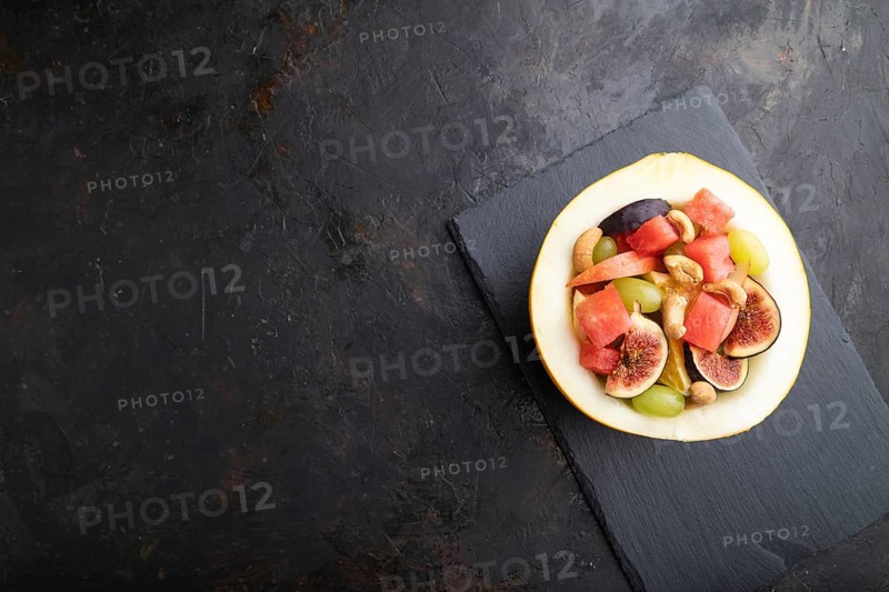Vegetarian fruit salad of watermelon, grapes, figs, pear, orange, cashew on slate board on a black concrete background. Top view, flat lay, copy space