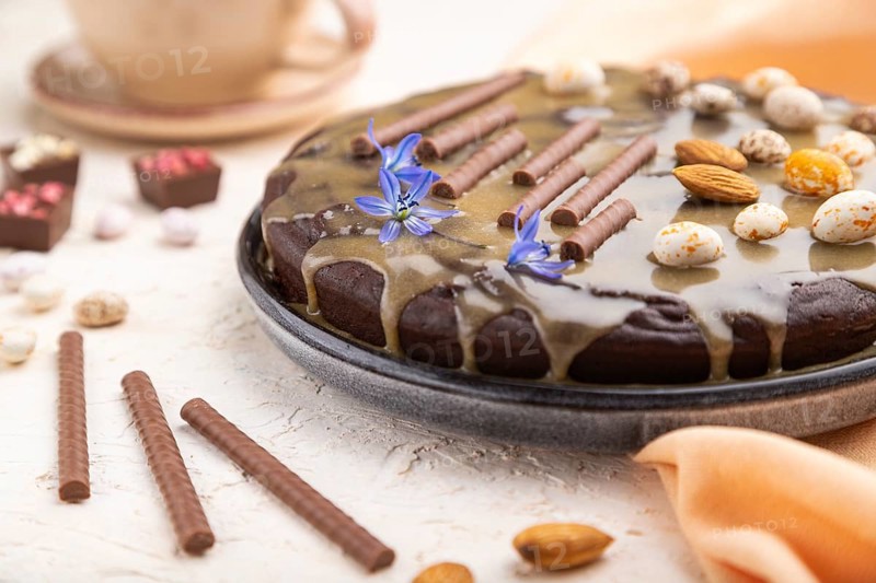 Homemade chocolate brownie cake with caramel cream and almonds with cup of coffee on a white concrete background and orange textile. Side view, close up, selective focus