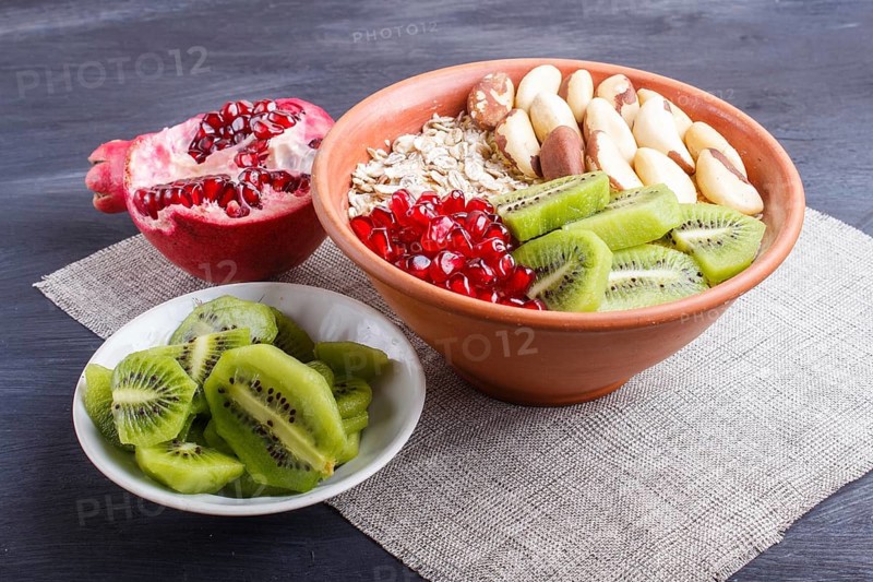 A plate with muesli, kiwi, pomegranate, Brazil nuts on a black wooden background. close up