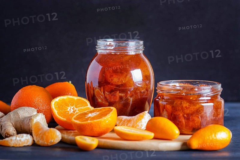 Tangerine and kumquat jam in a glass jar with fresh fruits on a black wooden table. Homemade, copy space, close up