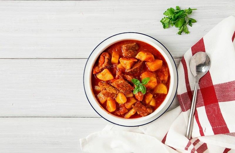 Geschmorte Kartoffeln mit Fleisch in Tomatensauce, mit Gewürzen und Kräutern, ohne Personen, auf einem weißen Tisch