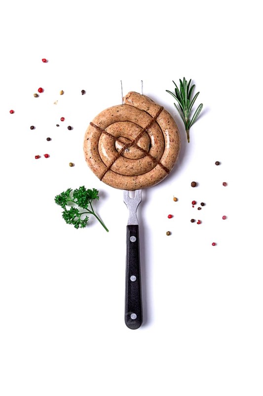 Raw spiral barbecue sausage, on a fork, on a white background, with spices and herbs, vertical, no people