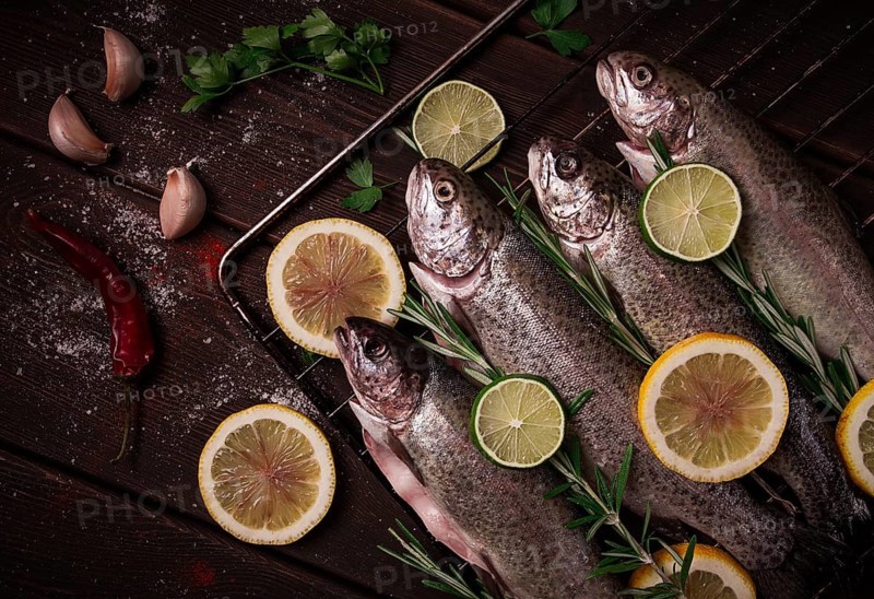 Raw rainbow trout, with lemon and herbs, on a wooden table, no people