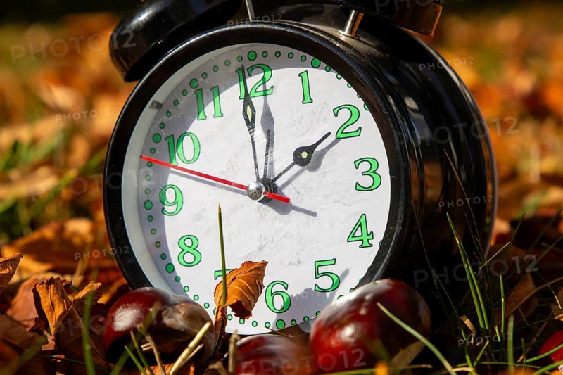 Symbolic image time change, autumn: An alarm clock among autumn leaves