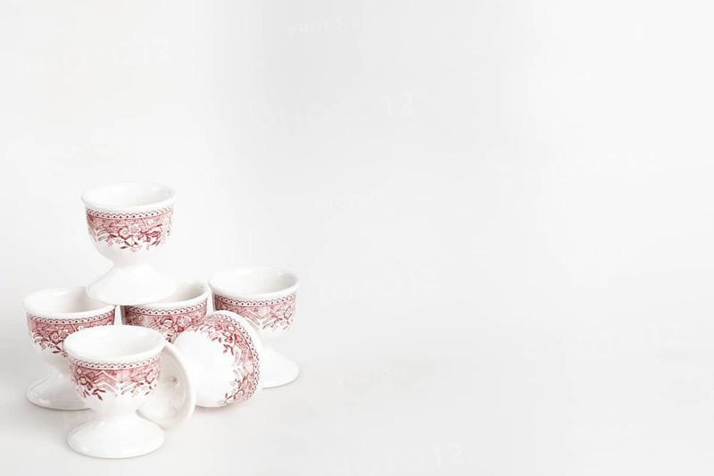 Ceramic egg cup with reddish pattern on white background, copy room