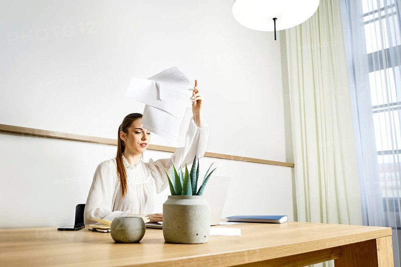 A woman is tired of monotonous work in the office and throws away documents