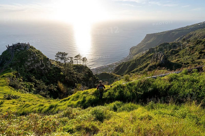 Young man looking out to sea on cliff, evening mood, green coastal landscape on cliff, sea and coast, viewpoint Miradouro da Raposeira, Paul do Mar, Madeira, Portugal, Europe