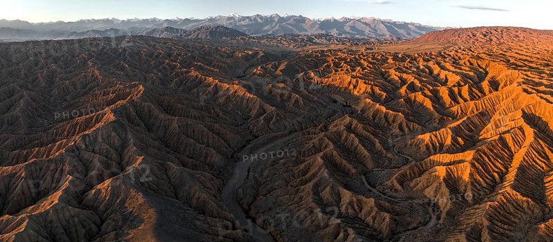 Landscape of eroded hills at Lake Issyk Kul, badlands at sunrise, mountain peaks of the Tien Shan Mountains in the background, aerial view, Canyon of the Forgotten Rivers, Issyk Kul, Kyrgyzstan, Asia