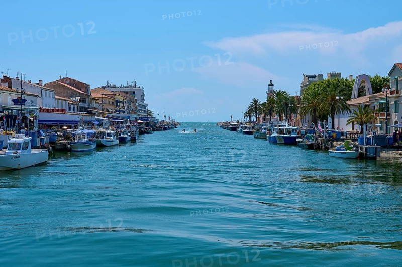 Coastal town with colourful houses, boats in the water and a lighthouse in the background on a sunny day, summer, Le Grau-du-Roi, Gard, Mediterranean Sea, France, Europe