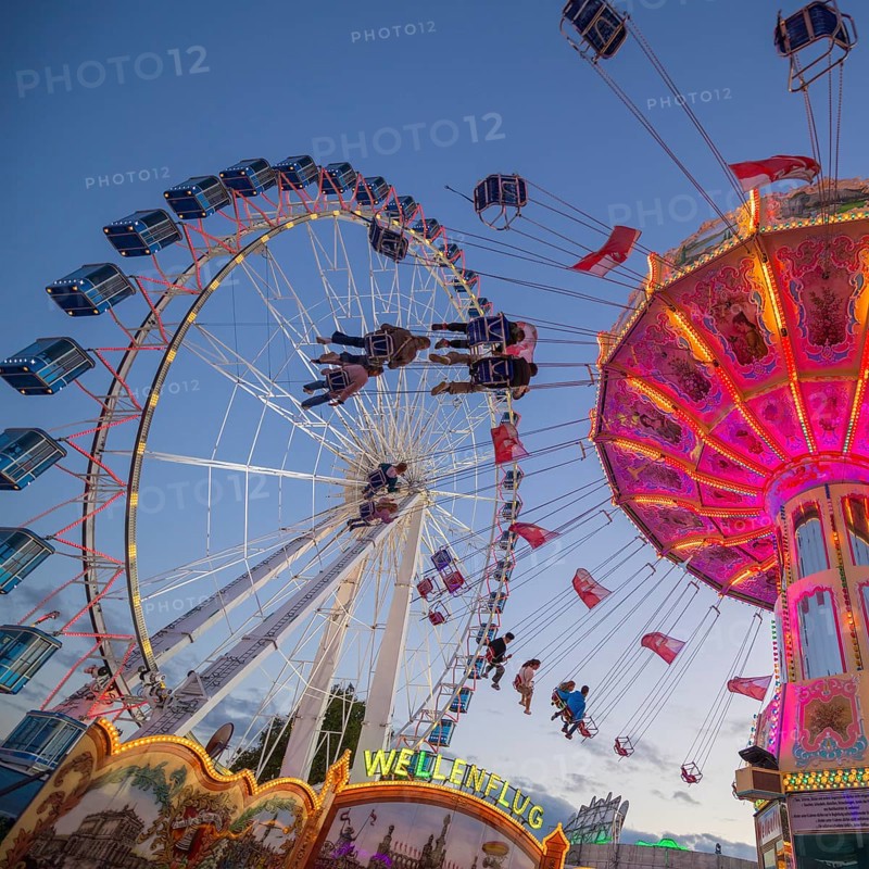 A funfair at dusk with illuminated chain carousel and Ferris wheel, Europa Rad, rides, wave flight, Cannstatter Wasen, folk festival, Bad Cannstatt, Stuttgart, Baden-Württemberg, Germany, Europe