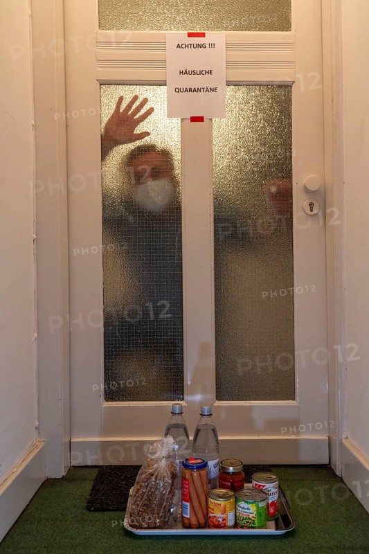 Symbolic image Domestic quarantine, man is in isolation at home due to a suspected corona infection, warning sign for visitors on the front door, communicating with a visitor through the door, neighbours have placed food in front of the door