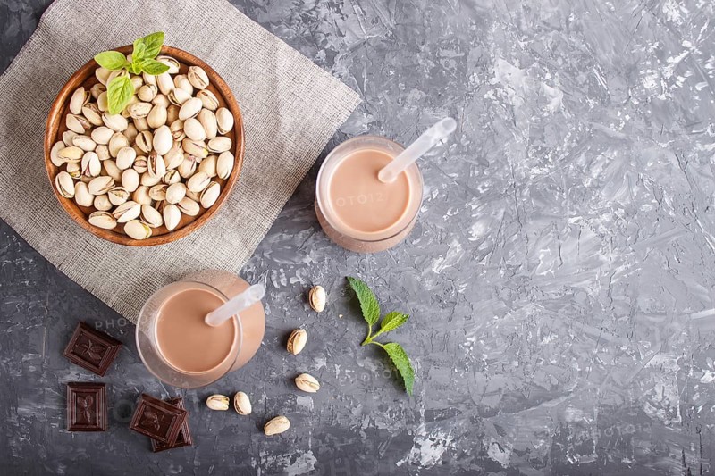 Organic non dairy pistachio milk in glass and wooden plate with pistachionuts on a black concrete background. Vegan healthy food concept, flat lay, top view, copy space