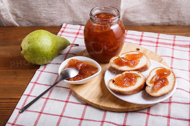 Pear jam in a glass jar on a linen tablecloth on a wooden table. Homemade, copy space