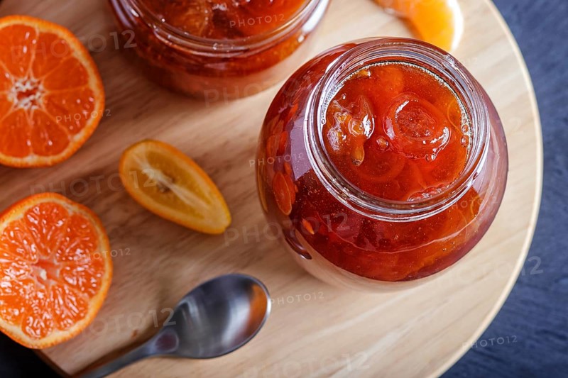 Tangerine and kumquat jam in a glass jar with fresh fruits on a black wooden table. Homemade, close up, top view