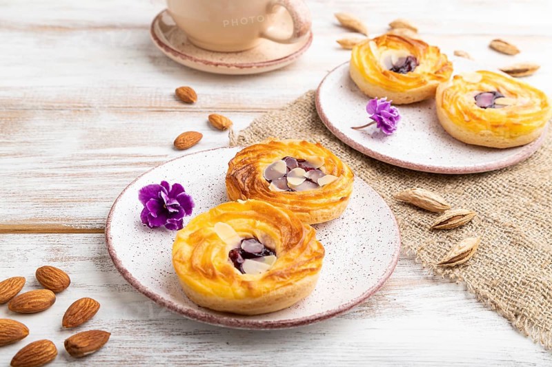 Small cheesecakes with jam and almonds with cup of coffee on a white wooden background and linen textile. Side view, close up