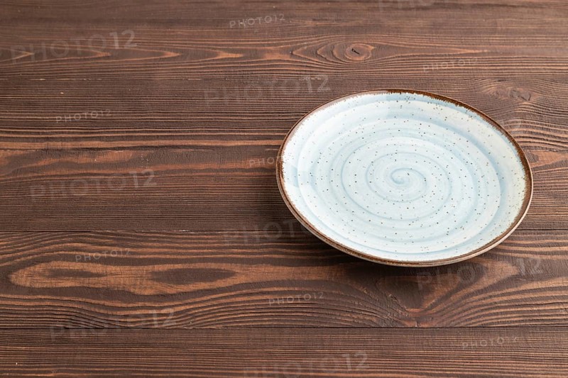 Empty blue ceramic plate on brown wooden background. Side view, copy space