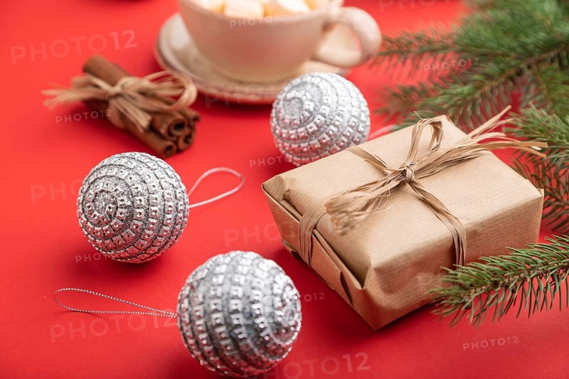 Christmas or New Year composition. Decorations, box, cinnamon, silver balls, fir and spruce branches, cup of coffee, on a red paper background. Side view, close up, selective focus