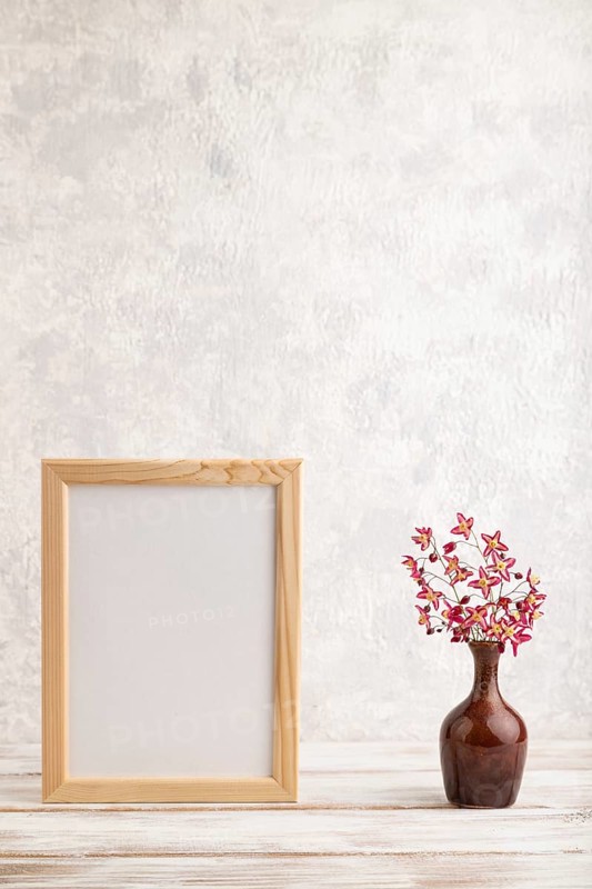 Wooden frame with purple barrenwort flowers in ceramic vase on gray concrete background. side view, copy space, still life, mockup, template, spring, summer minimalism concept