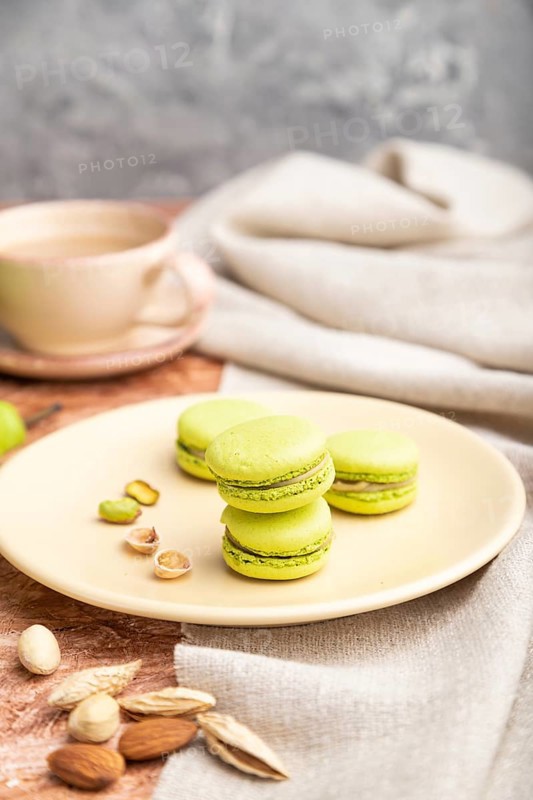 Green macarons or macaroons cakes with cup of coffee on a brown concrete background and linen textile. Side view, close up, selective focus