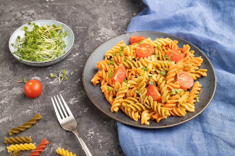 Tortiglioni semolina pasta with tomato and microgreen sprouts on a black concrete background and blue textile. Side view, close up, copy space