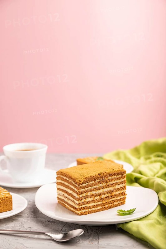 Homemade honey cake with milk cream and mint with cup of coffee on a and pink background and green textile. Side view, copy space, selective focus