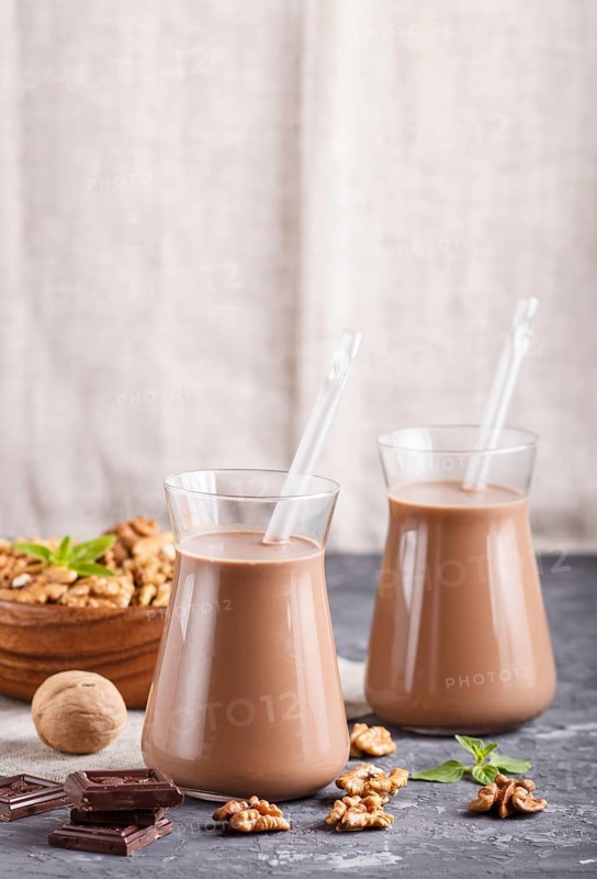 Organic non dairy walnut chocolate milk in glass and wooden plate with walnuts on a black concrete background. Vegan healthy food concept, close up, side view, copy space